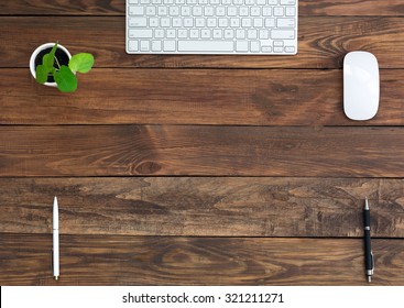 Brown Wooden Desk With Stationery And Electronics
Natural Wood Background Small Green Plant Computer Mouse And Keyboard Black And White Pens Top View