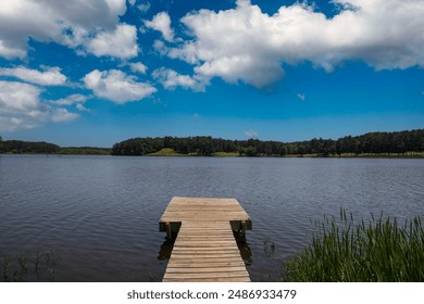 a brown wooden dock over the rippling blue waters of Lake Acworth surrounded by lush green trees and blue with powerful clouds at sunset at Cauble Park in Acworth Georgia USA - Powered by Shutterstock