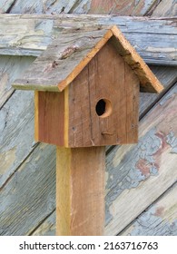 Brown Wooden Rustic Birdhouse On Post In Front Of Background Of Old Gray Weathered Barnwood