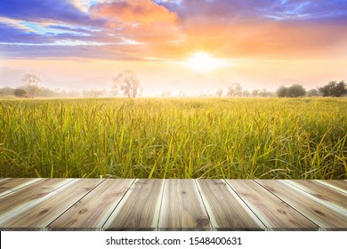 Brown Wooden Table Board Empty On Beautiful Organic Paddy-field. Rice Field And Sky Background At Sunset Time With Sun Rays.