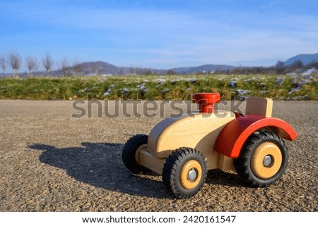 Brown wooden tractor with red steering wheel, toy tractor on a German asphalt road in winter in sunshine