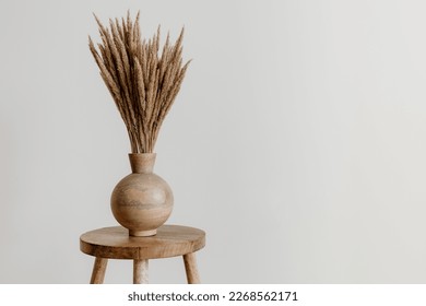 Brown wooden vase on a natural mango wooden stool with dried flowers in an empty room - Powered by Shutterstock