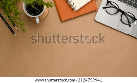 A brown workspace background with office supplies, laptop computer, eyeglasses, coffee cup and copy space for product display. top view
