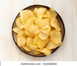 brown yellow chips from natural potato in brown ceramic plate on white wooden background, top view, close-up