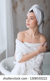 Brown-haired Young Woman In A Bathrobe, Standing Turned With Bare Shoulders, Prepares Buble Bath