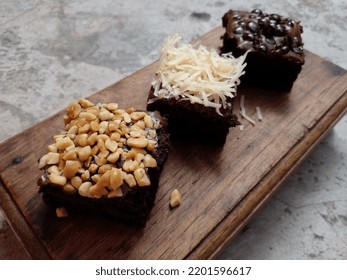 Brownie Cake Laid Out On A Wooden Cutting Board. Brownie Cake Topping With Nuts, Cheese And Choco Chips. Closeup Photo.