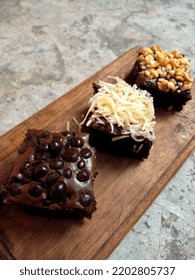 Brownie Cake Laid Out On A Wooden Cutting Board. Brownie Cake Topping With Nuts, Cheese And Choco Chips. Closeup Photo.