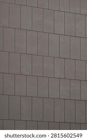 Brownish grey architectural cladding panels forming a minimal geometric background on a building facade.