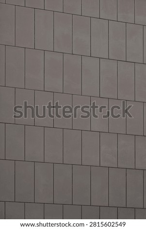 Brownish grey architectural cladding panels forming a minimal geometric background on a building facade.