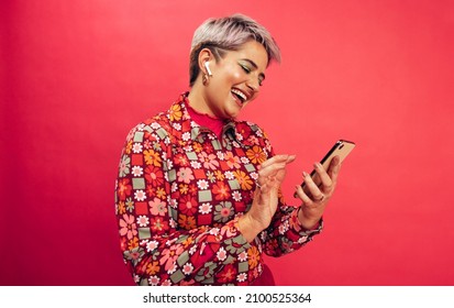 Browsing a popular music app. Happy young woman smiling cheerfully while holding a smartphone and wearing wireless earphones. Young woman with dyed hair enjoying her favourite music.
