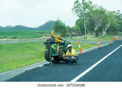 Bruce Highway Mackay to Townsville, Queensland, Australia - November 2021: A road construction worker crouches beside a machine while it drills a hole in the asphalt on the side of the road