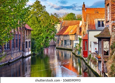 Bruges, Belgium. Medieval ancient houses made of old bricks at water channel with boats in old town. Summer sunset with sunshine and green trees. Picturesque landscape.