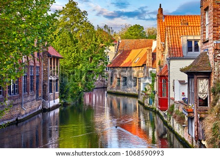 Bruges, Belgium. Medieval ancient houses made of old bricks at water channel with boats in old town. Summer sunset with sunshine and green trees. Picturesque landscape.