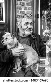 Bruges, Belgium,15/05/2019 Old Retired Grey Haired Bearded Man Smoking A Pipe With A Well Behaved Dog Sat On The Lap Drinking Outside A Pub Beer Cafe Cigarette Pensioner Retired Relaxing Chill