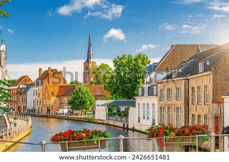 Bruges cityscape, Sint Annarei water canal, houses buildings on promenade in Brugge old town, flowers pots on fence, Bruges city historical centre, Saint Anna Church tower, Flemish Region, Belgium