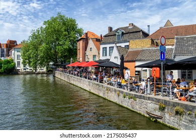 Brugge, Belgium - May 15, 2022: View Over Water Canal With Outdoor Terrace Restaurant, Green Trees, Blue Sky.