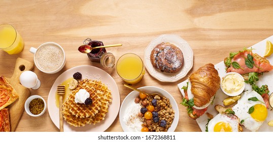 Brunch flatlay on wooden table. Healthy sunday breakfast with croissants, waffles, granola and sandwiches. Banner composition with copy space