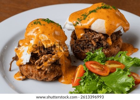Brunch plate featuring pulled pork eggs benedict with fresh vegetables and creamy sauce.