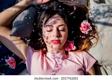 Brunet girl slipping in a bed with flwoer petals, shadows on a face. Above view
