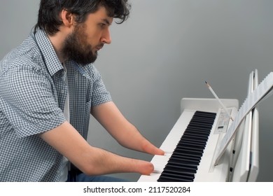 Brunet Man With Amputated Two Hands Is Playing The Piano. Life Of Guy Person Musician With Physical Disabilities. Composer Is Trying To Keep Playing And Creating Music After Injury And Writing Notes.