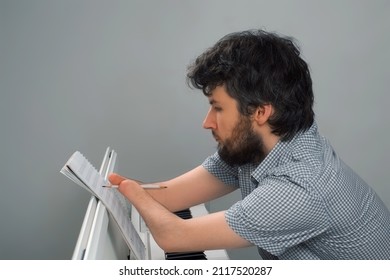 Brunet Man With Amputated Two Hands Is Playing The Piano. Life Of Guy Person Musician With Physical Disabilities. Composer Is Trying To Keep Playing And Creating Music After Injury And Writing Notes.