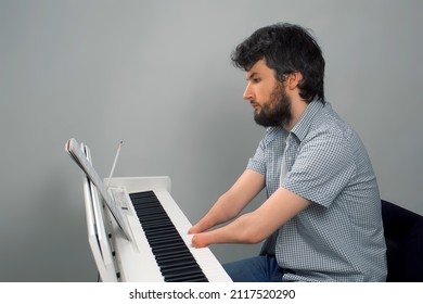 Brunet Man With Amputated Two Hands Is Playing The Piano. Life Of Guy Person Musician With Physical Disabilities. Composer Is Trying To Keep Playing And Creating Music After Injury And Writing Notes.