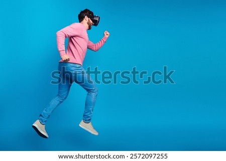 Brunet man experiencing virtual reality while jumping in casual wear against a vibrant blue background
