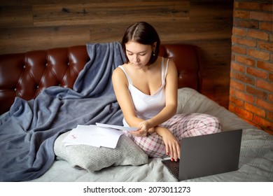 
piękna brunetka, praca na zlecenie, praca zdalna, nauka na odległość, płacenie rachunków, kursy finansów, dziewczyna na łóżku z laptopem i papierami, niezależna dziewczyna finansowa, feminizm - Shutterstock ID 2073011273