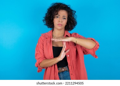 brunette arab woman wearing pink shirt over blue background feels tired and bored, making a timeout gesture, needs to stop because of work stress, time concept.