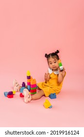 Brunette Asian Girl In Yellow Dress Playing Building Blocks On Pink