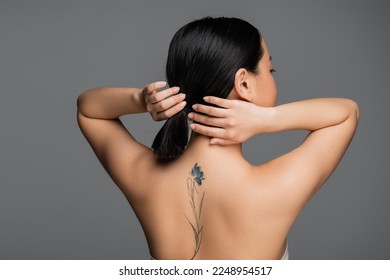 Brunette asian woman with tattoo on back touching ponytail isolated on grey - Shutterstock ID 2248954517
