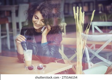 Brunette Beautiful Stylish Caucasian Woman In Casual Outfit On A Walk On European City Street Sitting At The Cafe Talking On Her Phone. Copy Space