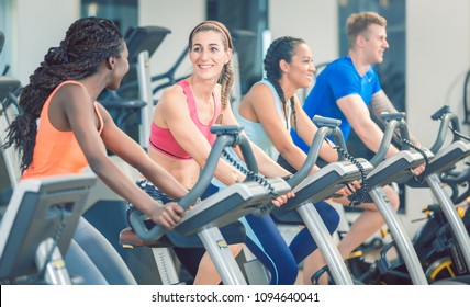 brunette hermosa mujer sonriendo mientras se monta en bicicleta en una moderna bicicleta de fitness durante la clase de spinning en el gimnasio