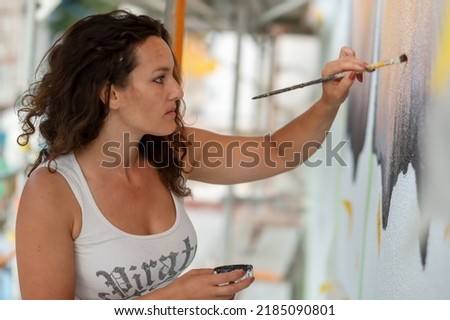 brunette beauty female artist woman in white shirt, with brush in front of a big mural, paints a butterfly on the wall, copy space