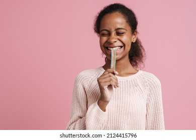 Brunette Black Girl Smiling While Eating Candy Worm Isolated Over Pink Background