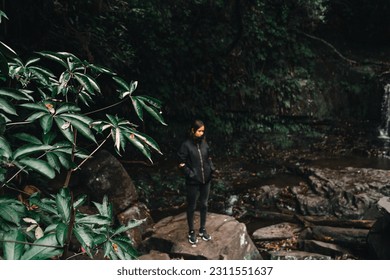 brunette caucasian girl in black jacket dark pants and sneakers out of focus calm and relaxed admiring the beauty of waterfalls and forest vegetation, purakaunui falls, new zealand - Shutterstock ID 2311551637