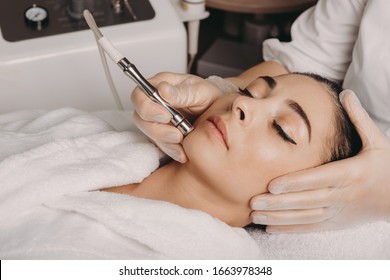 Brunette caucasian woman having a spa procedure for the skin of her face done with an apparatus by a spa worker