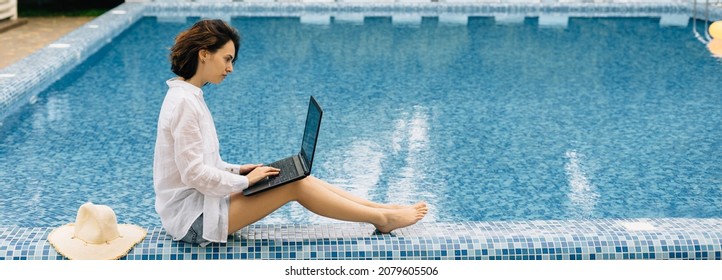 Brunette caucasian woman with laptop working near pool remotely freelancer. Online freelance work on vacation. The lady with the laptop is sitting by the water in her shirt. Place for text or banner. - Powered by Shutterstock