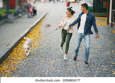 Brunette Couple Walking Their Golden Retriever Dog In The City On A Sunny Autumn Day