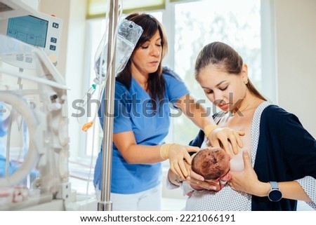 Brunette female breastfeeding consultant teaching new mom to breastfeed newborn baby in hospital room. Pain while feeding. Concept of lactation infant feeding.