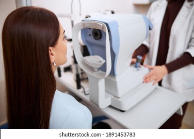 Brunette Female Sitting Straight On A Chair In Front Of An Automated Refractor After Having A Medical Examination