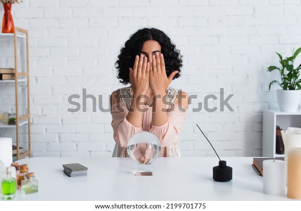 brunette fortune teller\
obscuring face with hands near magic orb and diffuser with aroma\
stick