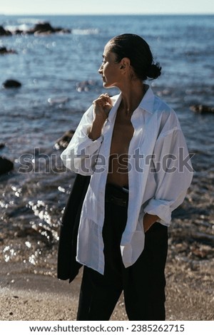 Brunette girl in a black men's suit barefoot on the beach by the
