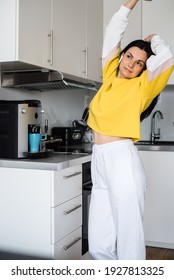 Brunette Girl With Bluetooth Headphones Dances In The Kitchen In The Morning And Makes Coffee In A Coffee Machine