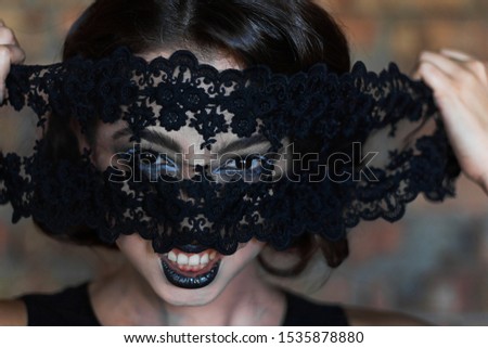 A brunette girl with creative make-up looks through black lace and shows different emotions. halloween concept