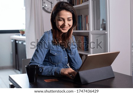 brunette girl with denim shirt sitting in the living room table buys online from her tablet thanks to her credit card
