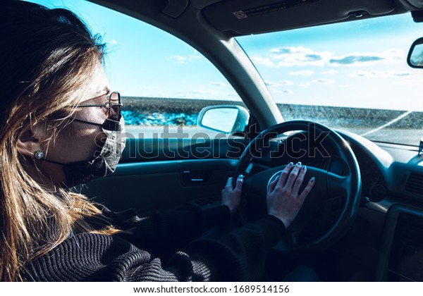 A brunette girl drives a car in a medical
mask, fearing infection.