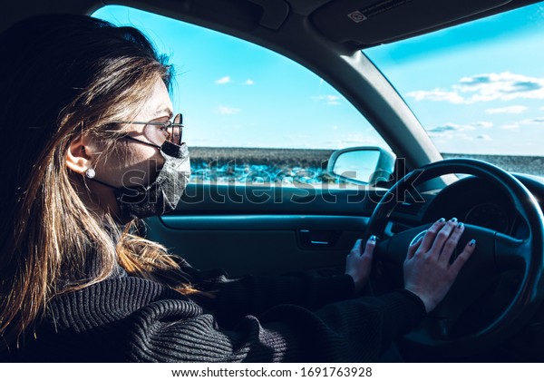 A brunette girl drives a car in a medical\
mask, fearing infection.