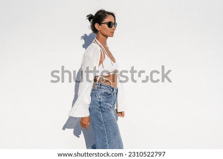 brunette girl in glasses in a white swimsuit and blue jeans agai