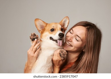 a brunette girl holds and hugs a red corgi dog on a clean light background, the concept of love for animals - Powered by Shutterstock